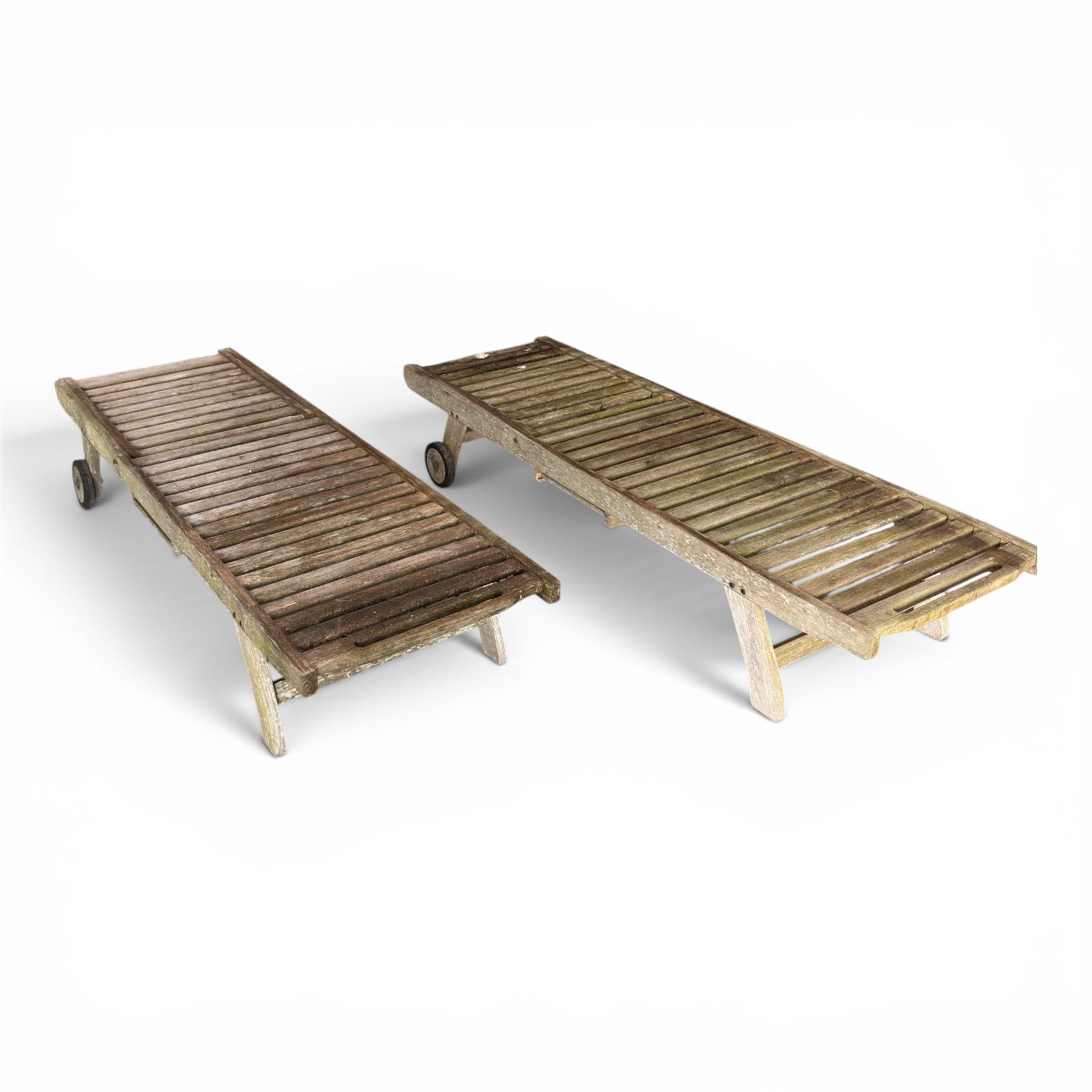 Pair of teak garden sun loungers, with slatted adjustable backrests, integrated wheels and sliding pull-out side trays, weathered natural finish.
