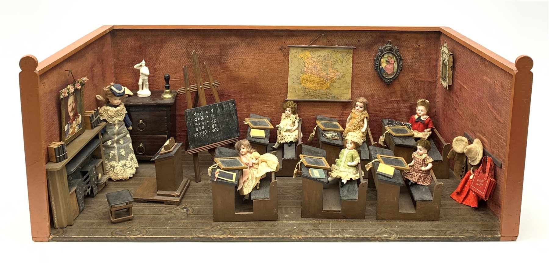 Late Victorian wooden school room setting with bisque head teacher and six German all bisque pupils each seated at a combined desk and chair with slate board, in a classroom furnished with chest of drawers, fire-surround, lectern, wall map, pictures, miniature books, school bell, chalk board on easel, wall clock etc, L70cm H28cm D28cm