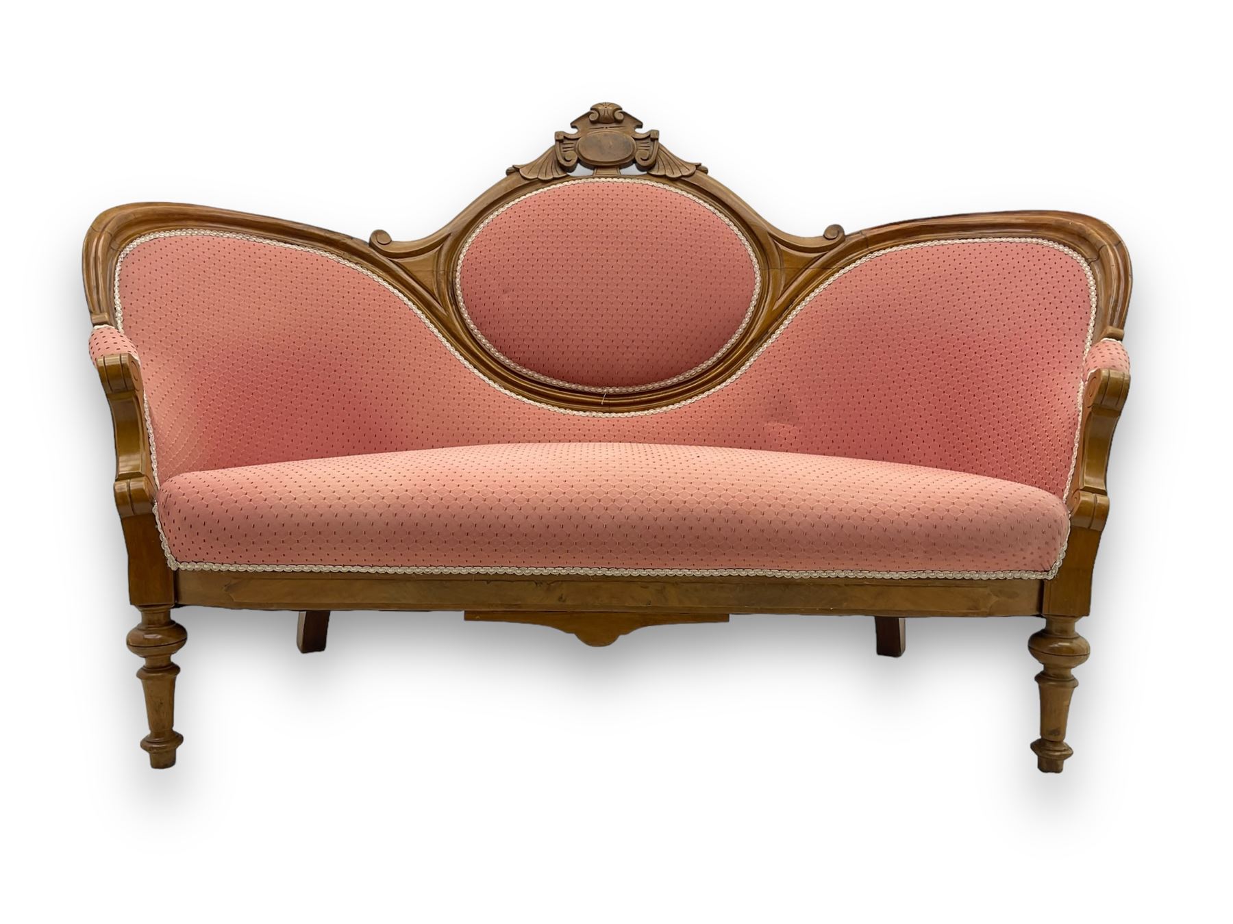 Late Victorian walnut framed double spoon back sofa, shaped crest rail with central carved medallion over curved back with pink upholstery, scrolling arms with additional carvings, on turned supports