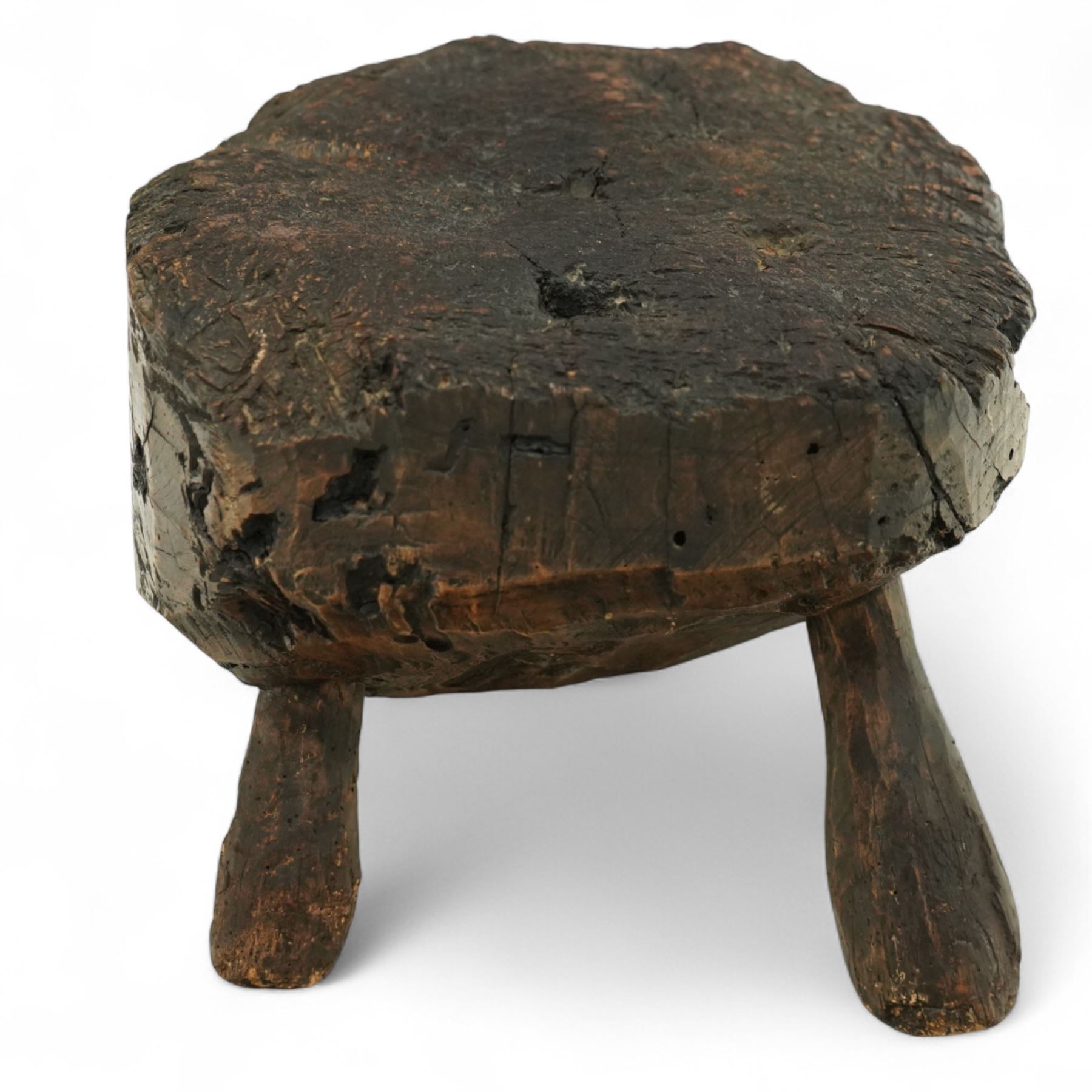 Rustic bog oak stool of oval form with a single solid section with a deeply patinated and textured surface, raised on three tapered stick legs, possibly Irish 