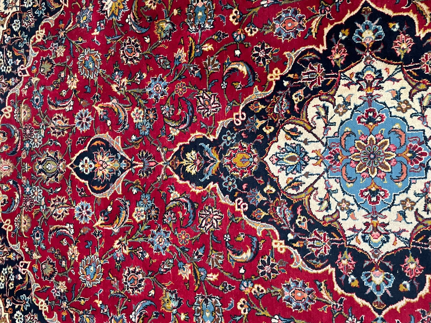 Persian Kashan crimson ground carpet, the central pole medallion decorated with flower heads, surrounded by trailing leafy branches and palmettes, scrolling border decorated with further palmettes, within floral pattern guard stripes 