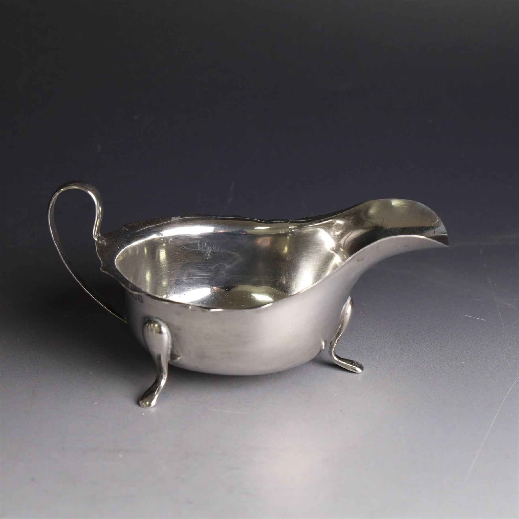 Three silver sauce boats, comprising pair of 1930s silver sauce boats, of typical form with shaped rim, scroll handle and upon three pad feet, hallmarked Viner's Ltd, Sheffield 1932 and a similar 1920s example with flying C scroll handle and upon three paw feet, hallmarked James Deakin & Sons, Sheffield 1923, tallest including handle H7.5cm