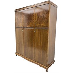 Early 20th century figured walnut triple wardrobe, banded cornice over three doors, each crossbanded with boxwood stringing and shaped figured oval panels over a blind-fretwork row with shell and scrolling decoration, on cabriole feet