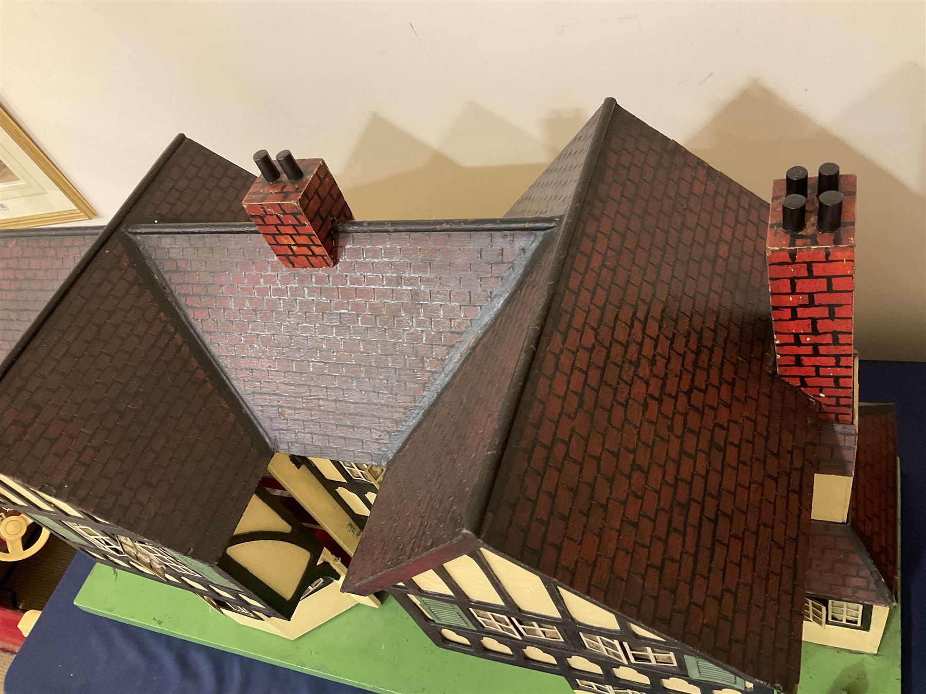 Large Tri-ang No.93 doll`s house in the 'Stockbroker's Range' c1935; two-storey double-fronted Tudor design, half timbered gables, two-storey bay windows, cream and mock shrubbery to front, opening metal framed windows with green shutters, red simulated tiled roof with chimney, integral garage with opening doors, front elevation has four hinged doors opening to reveal two bedrooms with fire places, living room, bathroom and kitchen with built in dresser and sink, entrance hall and staircase, side entrance with porch and seat and sun dial over on chimney stack; some wiring for electrical lighting; metal Tri-ang Toys disc verso; comprehensively furnished H66cm L117cm D43cm