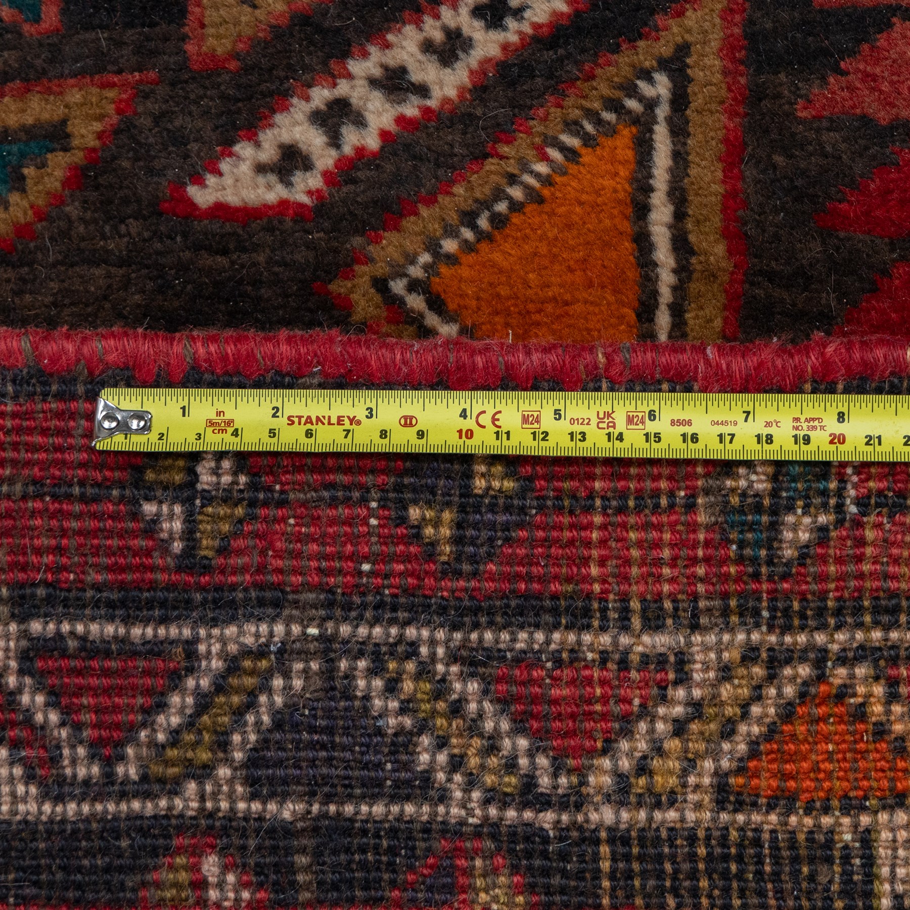 North East Persian Kurdie runner, the red field decorated with three serrated diamond medallions alternating with four ochre hooked motifs enclosing polychrome cruciform panels, within multiple geometric borders of repeating triangles and diamond devices