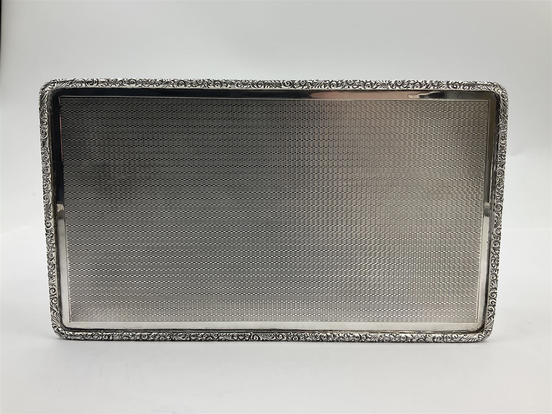 1920's silver table cigarette box, of rectangular form with engine turned decoration to the exterior, the hinged cover with central vacant rectangular panel and raised foliate rim, opening to reveal a gilt interior with later plush lining, hallmarked Charles Henry Dumenil, London 1923, H3.5cm L14.5cm D8.5cm