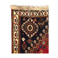Persian Qashqai crimson ground runner, the field decorated with repeating diamond-shaped medallions flanked by angular floral motifs, the spandrels with intricate boteh designs, framed by an ivory border with stylised floral patterns and scrolling vines