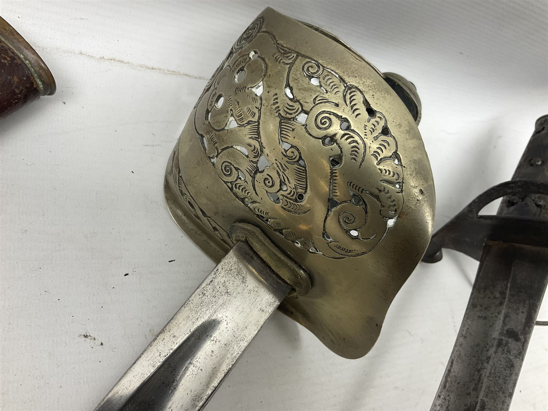 George V British Army 1897 pattern officers sword with plain 82cm fullered steel blade, pierced  basket hilt with George V cypher and wire bound leather grip with chequered backstrap; in leather covered field service scabbard L101cm overall; and another officer's sword in relic condition lacking scabbard (2)