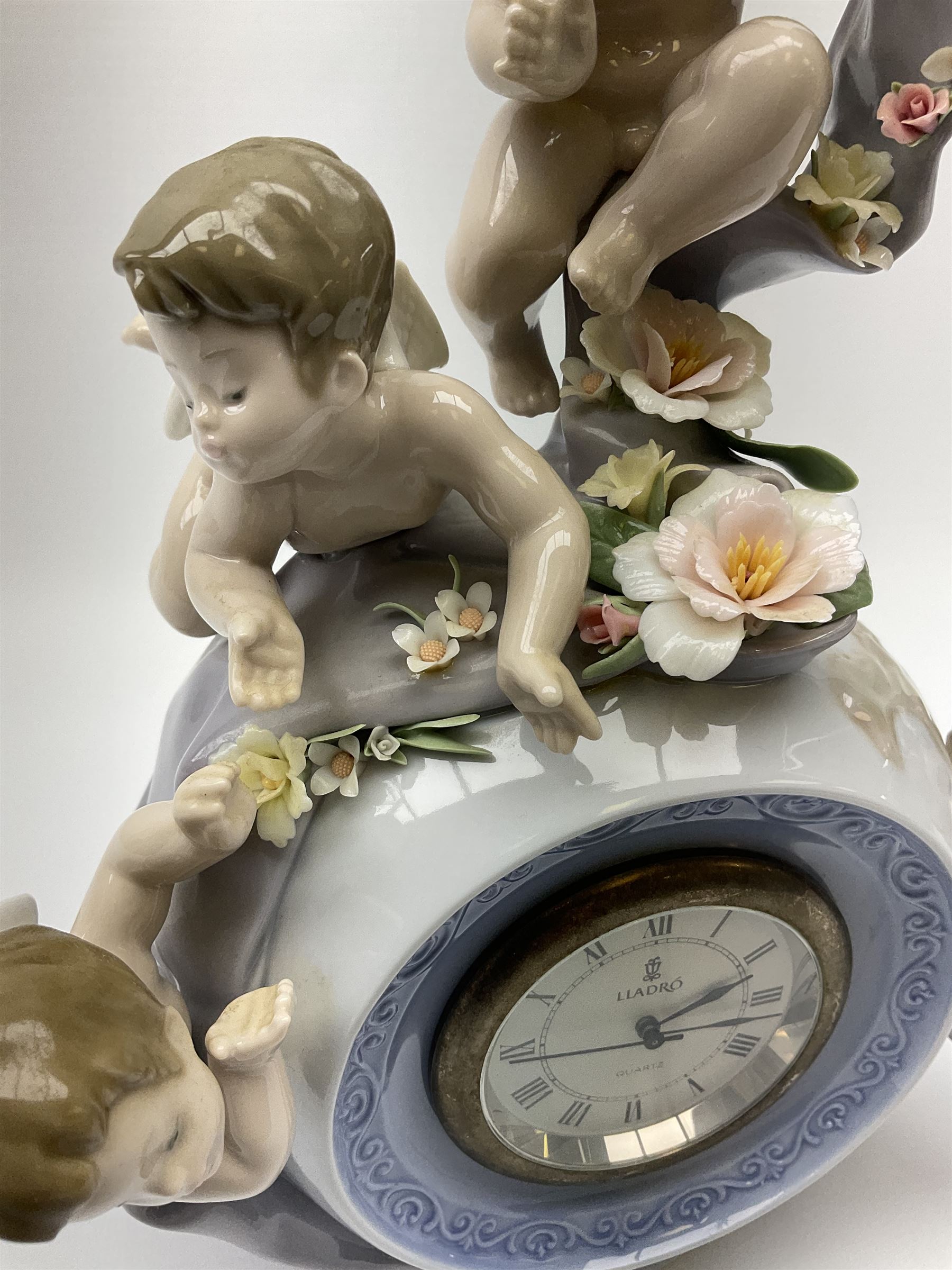 A Lladro mantel clock modelled as a globe with inset clock, surmounted by four putti and floral garlands, with blue printed mark and impressed 5973 beneath, H29cm.