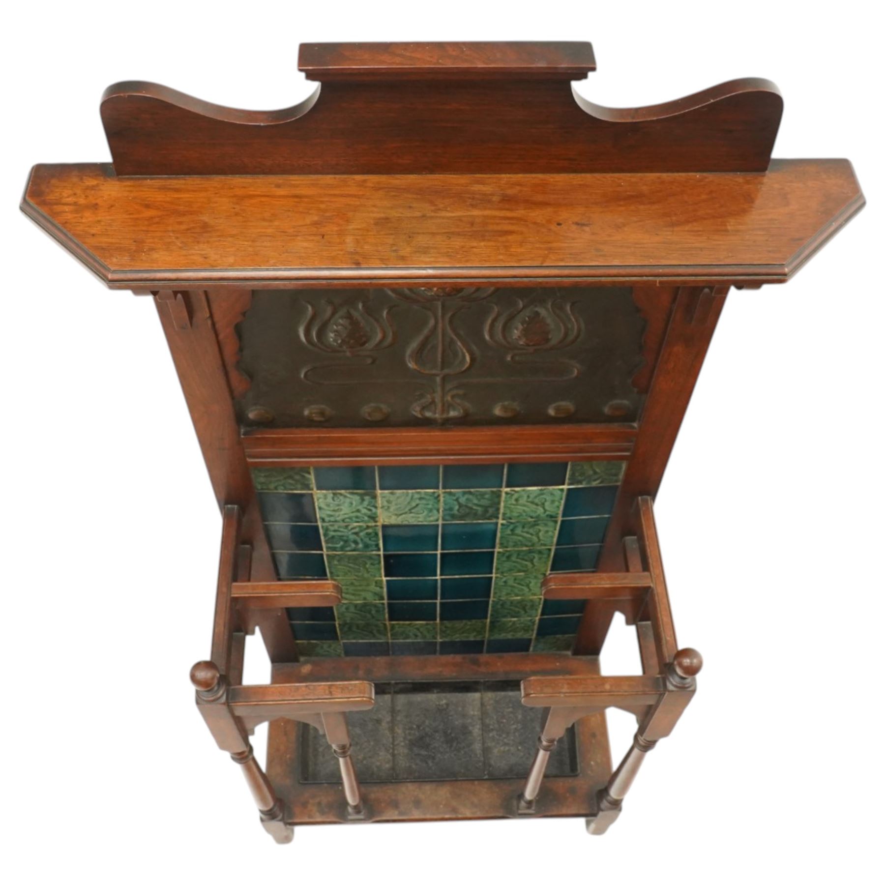 Shapland & Petter of Barnstaple - Arts & Crafts mahogany tile-backed umbrella or stick hall-stand, model no.114, the shaped back with single shelf over an Art Nouveau embossed patinated copper panel and turquoise tiled back, with turned supports and dividers over inset metal drip tray

Notes: A comparable Shapland & Petter stick stand of this model is recorded in Daryl Bennett, Shapland & Petter Ltd of Barnstaple, Museum of Barnstaple and North Devon, p.84, cat. no.5.37, and the model is also listed in Bennett, Liberty’s Furniture 1875-1915, p.298, cat. no.8.6. Examples of this model are known to have been retailed by Liberty & Co.