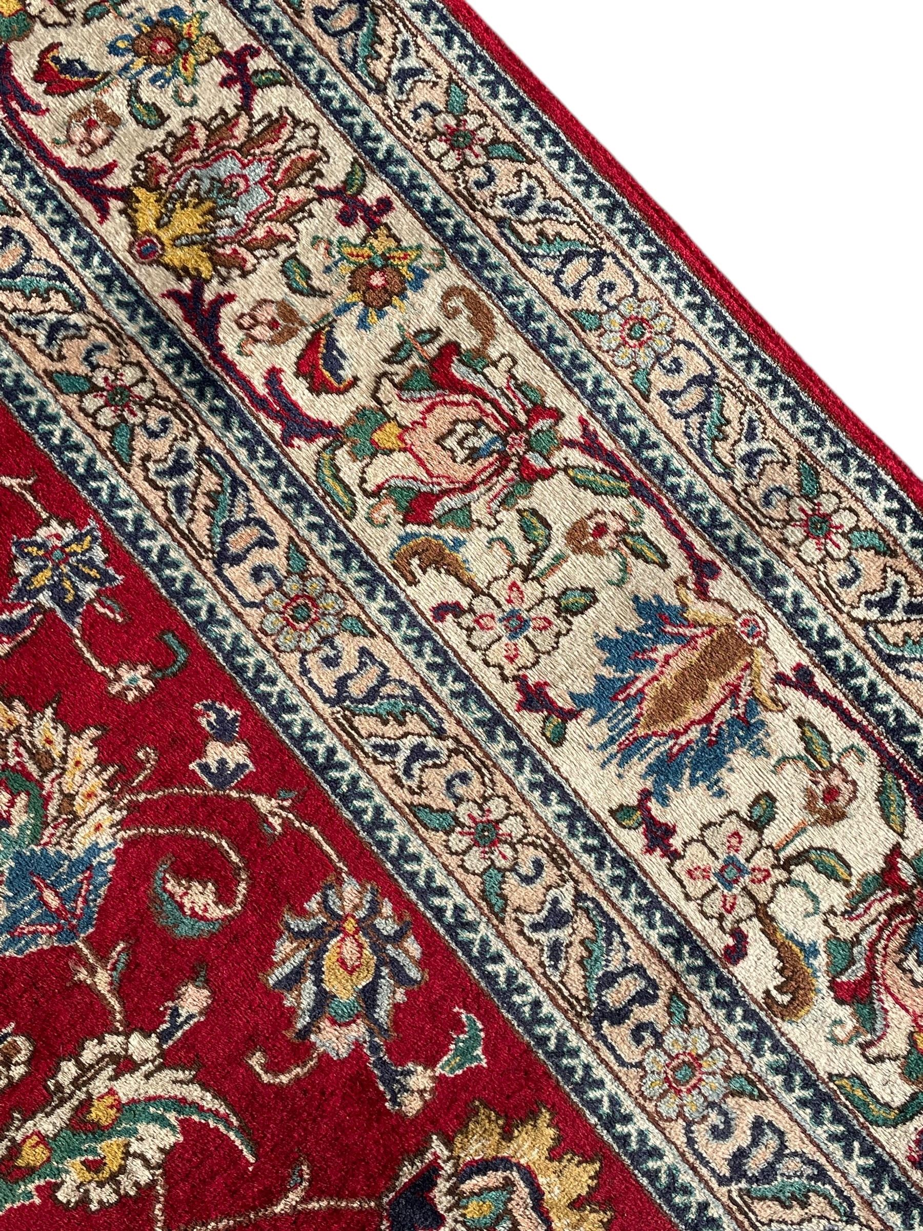 Persian Tabriz crimson ground carpet, decorated with swirling leafy branches and large palmette motifs, the pale ground border decorated with trailing foliate pattern, within floral guard stripes
