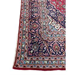 Central Persian Kashan crimson ground carpet, central  floral pole medallion with matching spandrels within a field of scrolling palmette motifs and foliage, the heavily banded indigo border with repeating plant motifs interlaced with scrolled branches