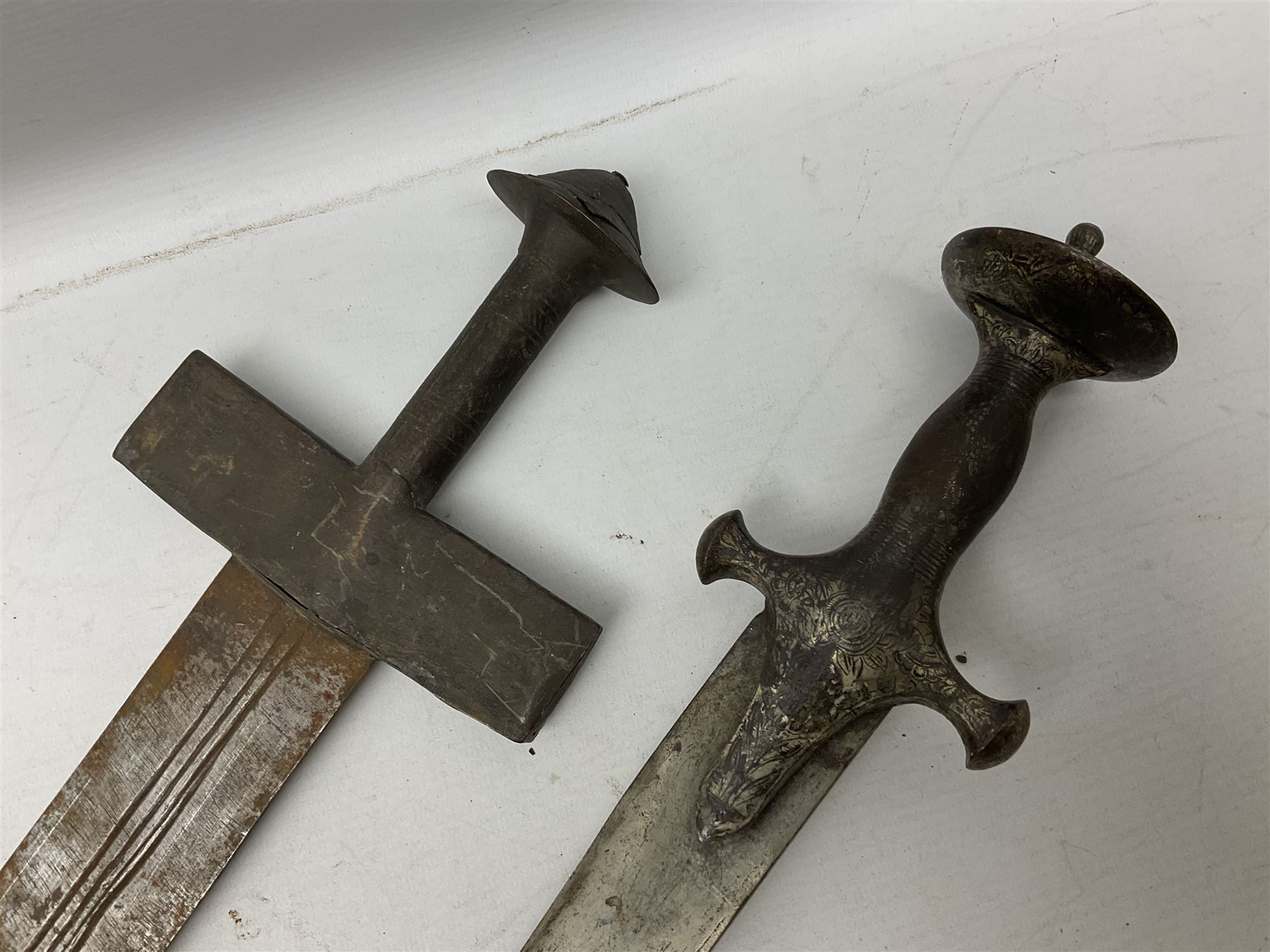Tuareg Takoba sword with 78.5cm triple fullered blade incised with two crescent moons to either side, metal hilt with stylised floral designs to the cross-guard, decorative grip and disc form pommel cap; in tooled leather scabbard decorated with geometric designs L92cm overall; and an Indian Tulwar sword with 75cm plain curving blade and 'silver' damascened hilt (no scabbard) (2)