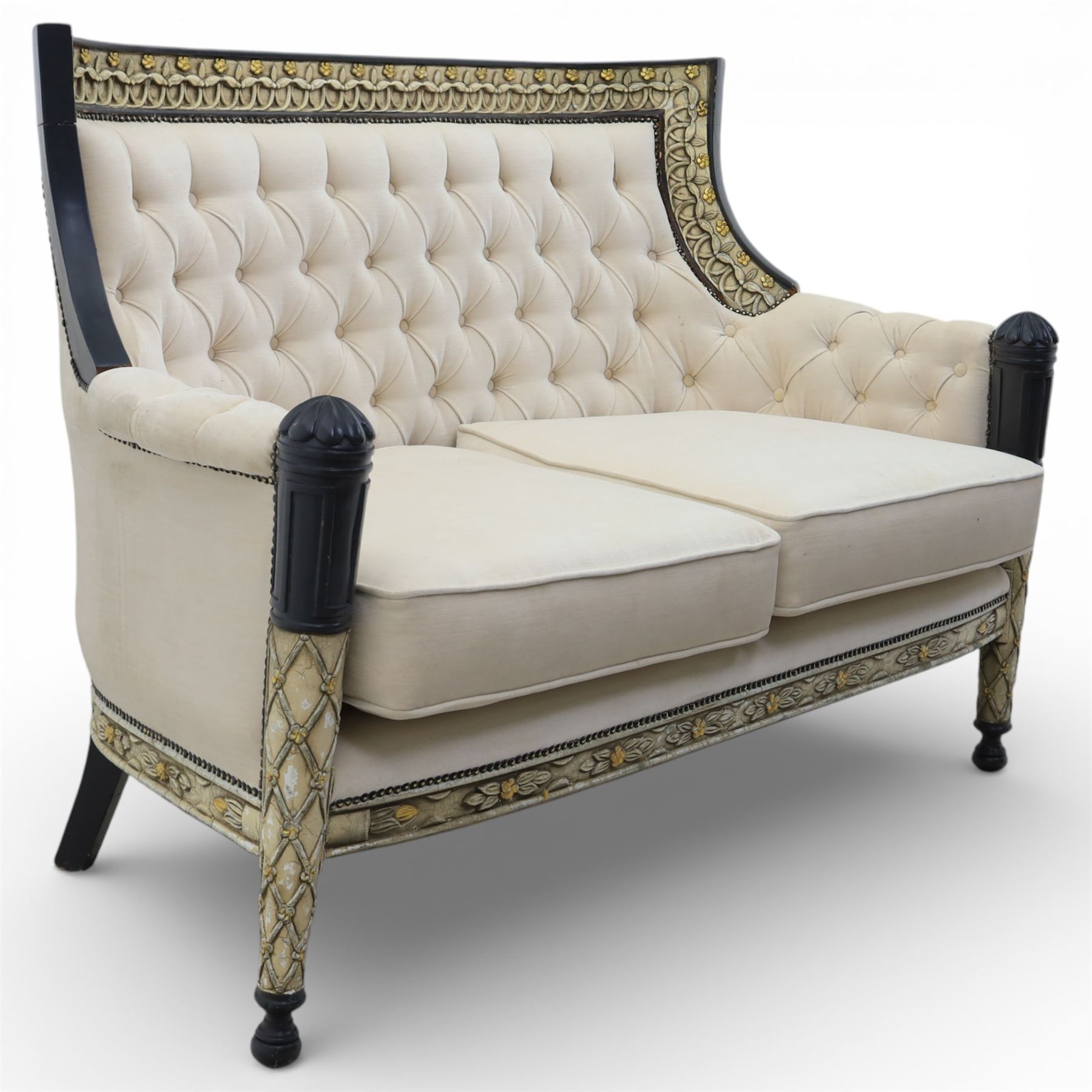 20th century Louis XVI style settee, upholstered in cream fabric with buttoned back and arms, and plain seat cushions, the shaped and black painted frame with entwined foliate detail and gilt flower heads, upon column legs with bun feet