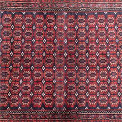 North East Persian Turkoman hand-knotted rug, indigo field densely decorated with an all-over repeating design of geometric gul motifs in shades of madder red, aubergine, and dark brown, highlighted with small ivory details, framed by multiple narrow guard borders and a main border with angular geometric motifs flanked by zig-zag borders, with cotton fringe ends 