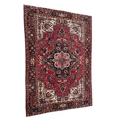 Persian Heriz red ground rug, central scrolled medallion on dark ground decorated with floral motifs, the surrounding field decorated with stylised plant motifs and smaller geometric symbols, guarded border with repeating pattern punctuated with rosettes and flower heads 