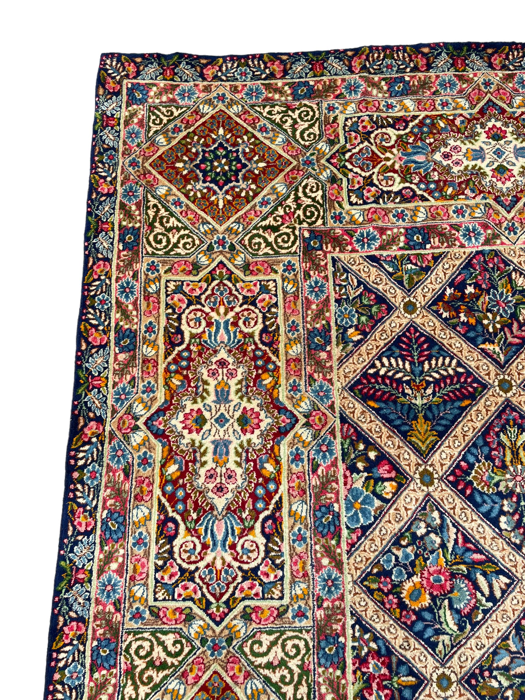 Persian Kirman indigo ground carpet, the field with repeating lozenge tiles with overall floral decoration, the main border with floral panels enclosed by the guards