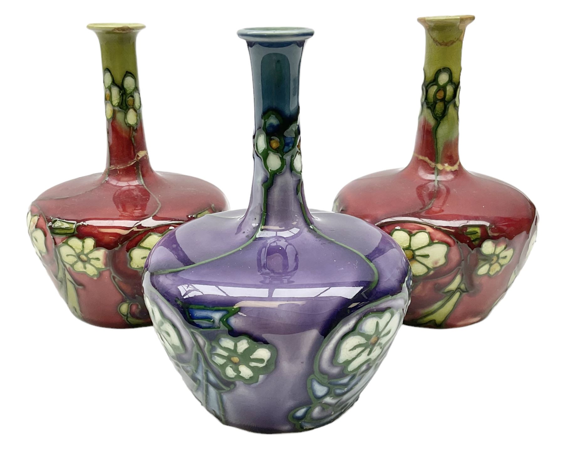 Three Minton Secessionist vases, with tube-lined stylised flower decoration, two upon a red ground and third upon a purple ground, all with printed mark to base 'Minton Ltd, No. 33', H13cm