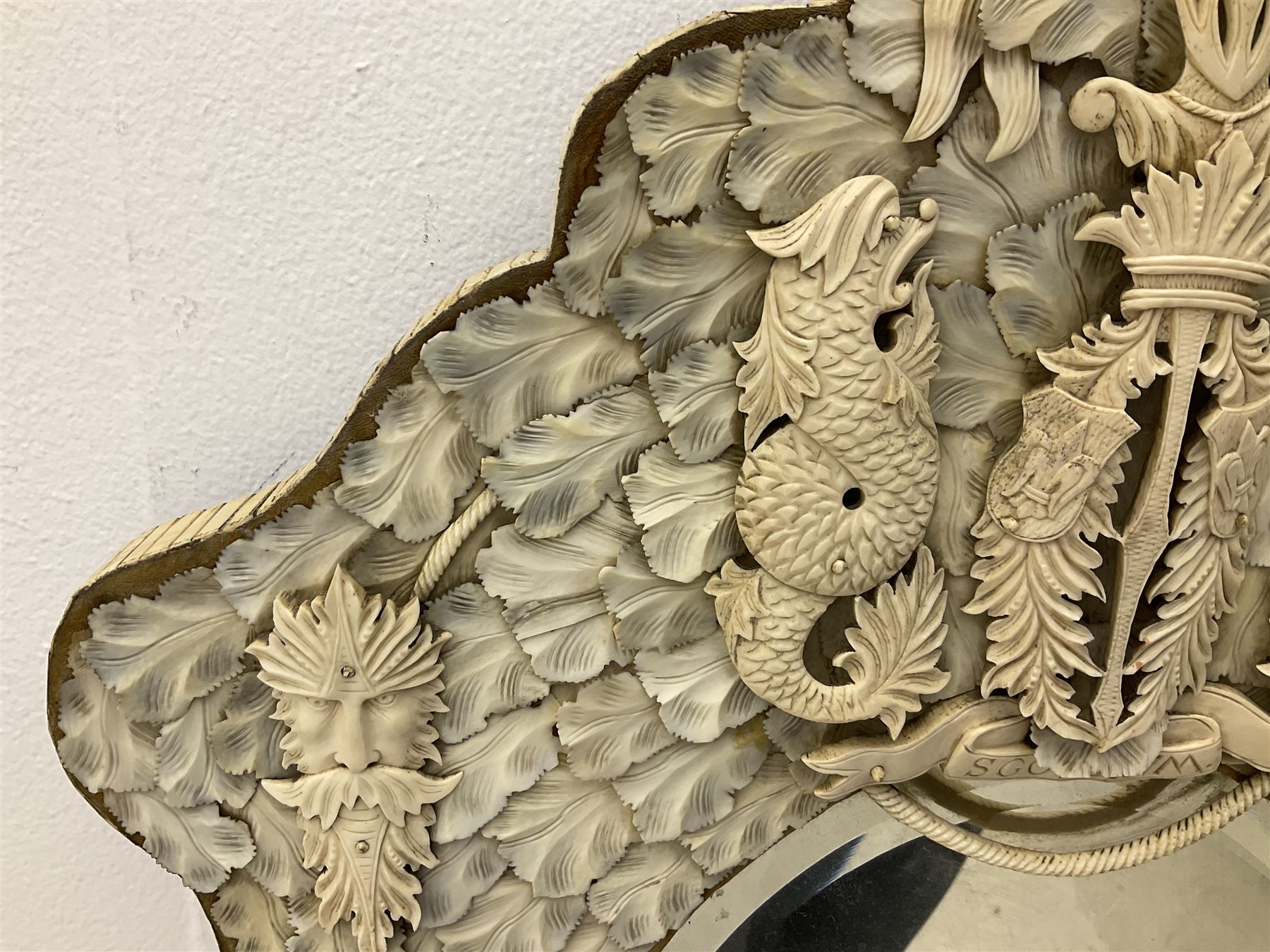 Pair 19th century French Dieppe bone and ivory wall mirrors, the oval bevelled mirror plates within rectangular frames with shaped tops, profusely decorated with ivory leaves, further detailed with carved bone armorial type crest inscribed 'SGOTORVM', putti, fish and mask heads, H81cm W48cm