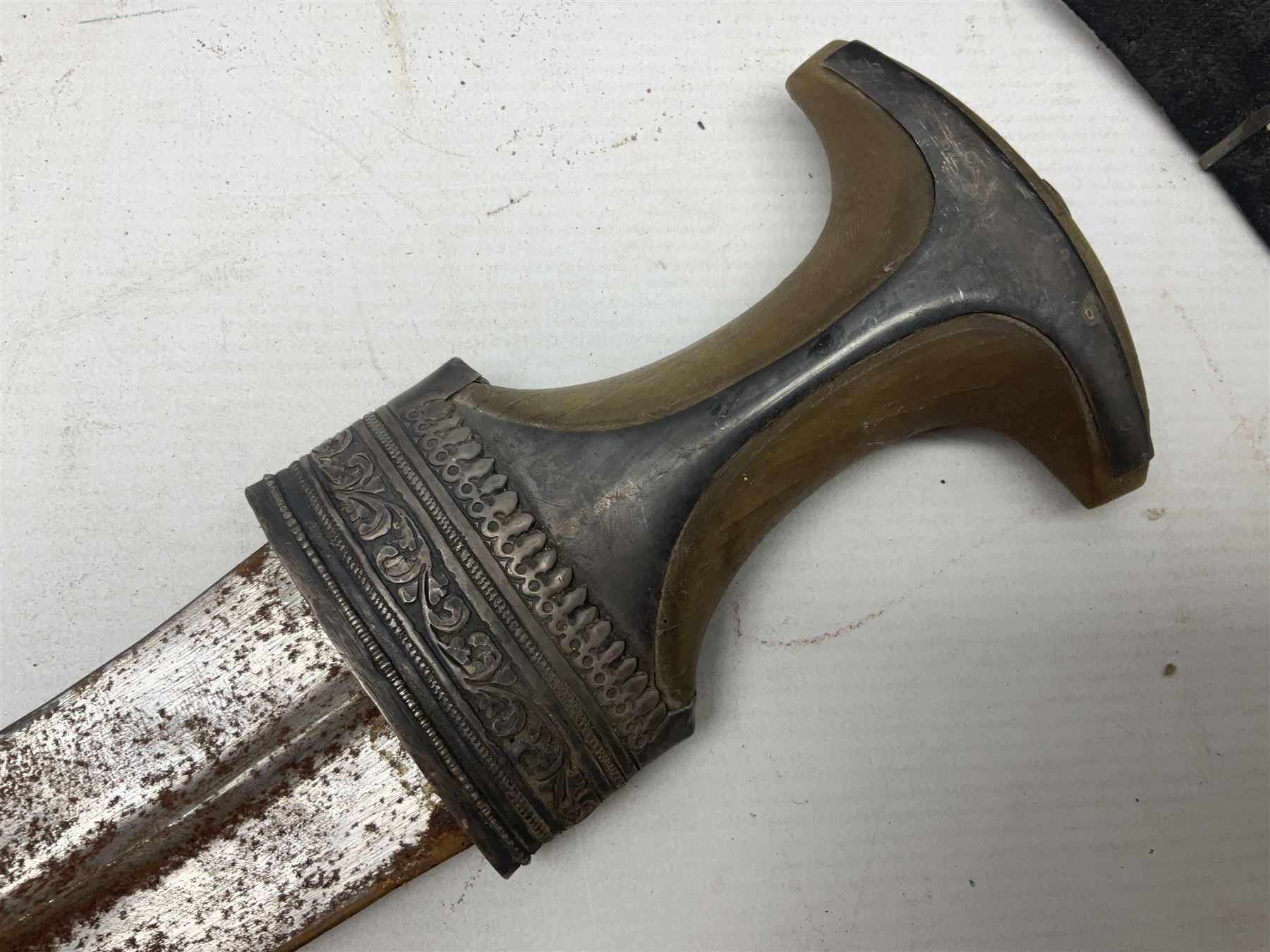 Omani Khanjar dagger, the 19cm curved blade with pronounced medial rib to either side, waisted hilt with dome shaped pommel and silver mounted horn grip decorated with an embossed band; in an intricately decorated silver scabbard with silver rings woven into the belt mount and fitted with original coin mounted silver thread-work belt with additional side knife in sheath verso L34cm overall, belt length 81cm; together with a Nepalese kukri in leather scabbard with one skinning knife (2)