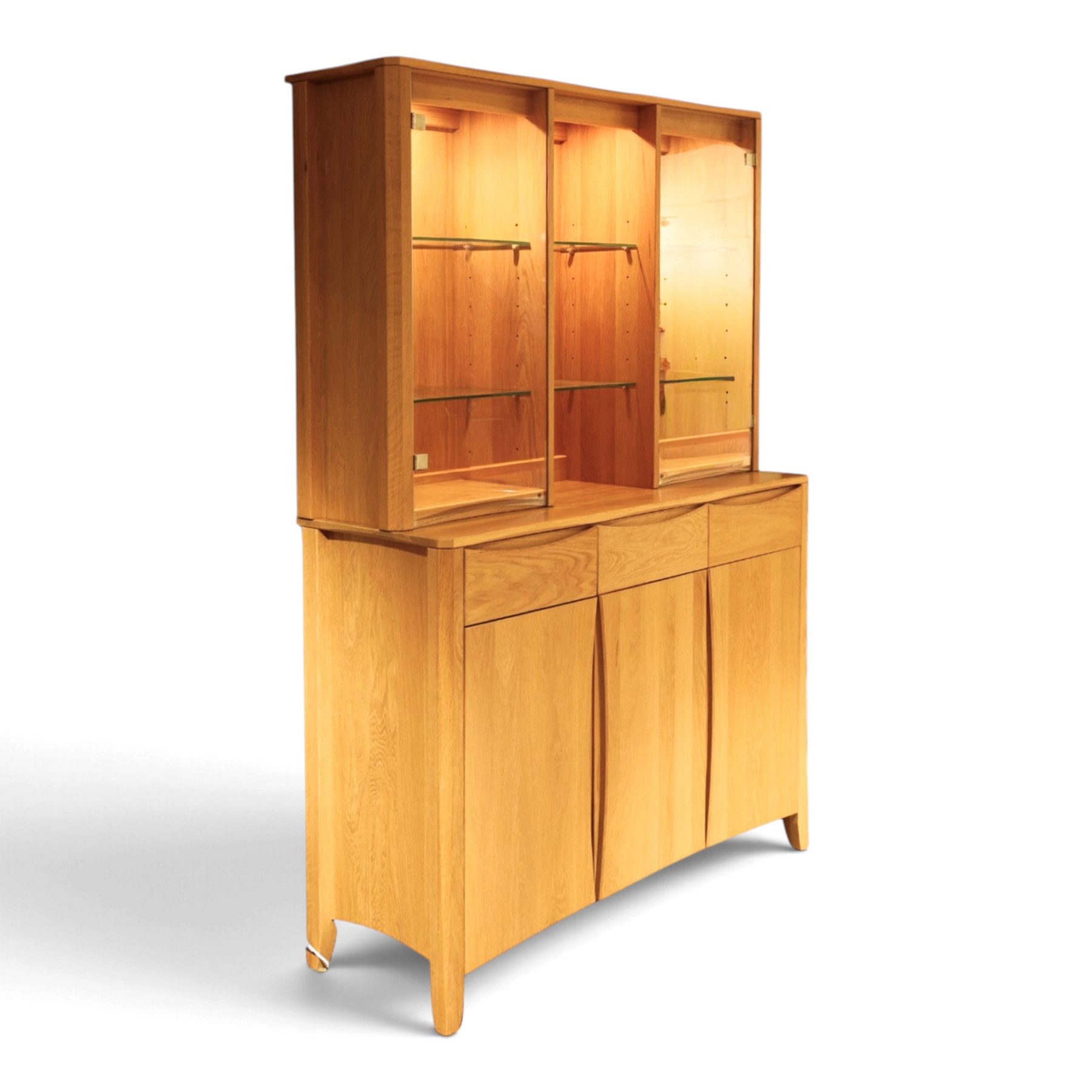 Ercol - 'Artisan' light oak dresser, upper section with cantered corners, with central open area fitted with adjustable glass shelves, flanked by twin glazed cabinets with further adjustable glass shelving, the lower section with three shorts drawers with recessed handles, above three cupboard doors with recessed handles enclosing adjustable wooden shelves, raised on short tapering supports 