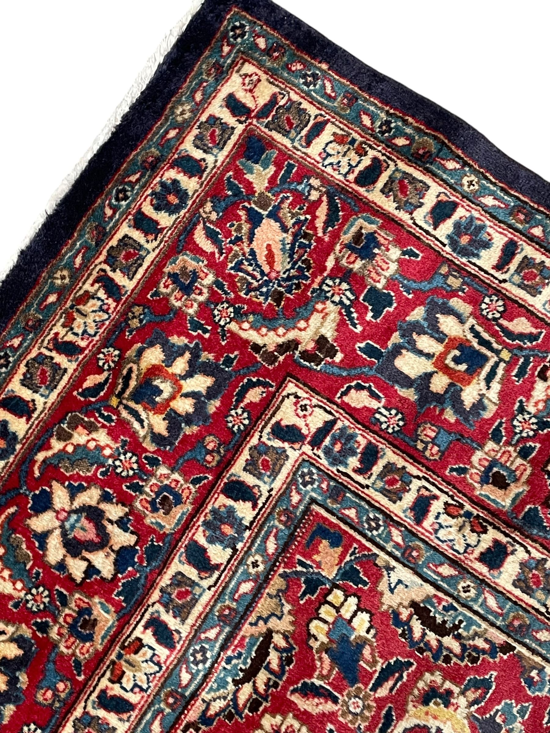 Persian Kashan indigo ground carpet, large central rosette medallion decorated with alternating palmettes, the surrounding field and spandrels with overall floral design depicting trailing branches and stylised plant motifs, crimson ground border with trailing floral pattern, enclosed within guard stripes 