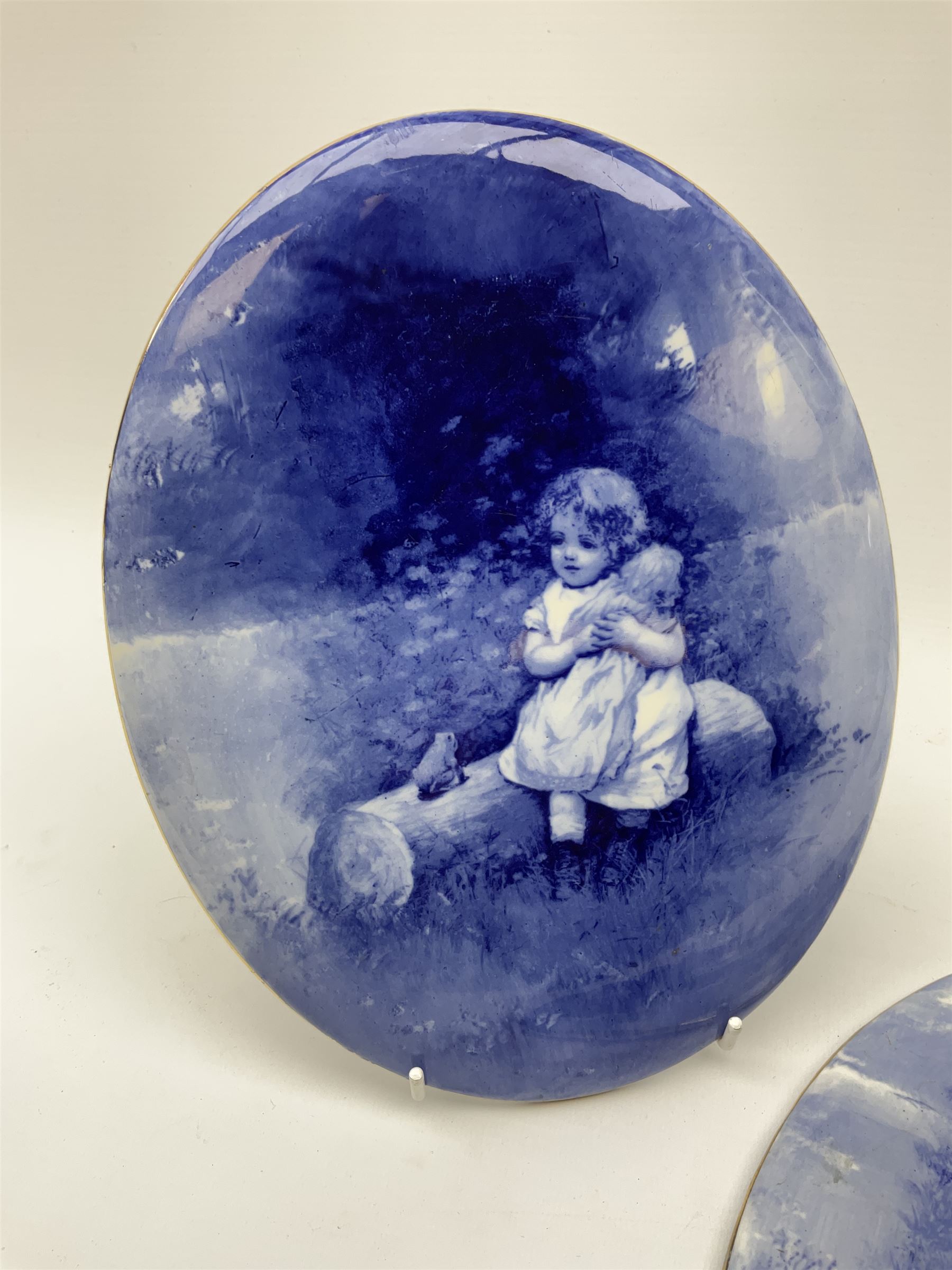 A pair of Royal Doulton blue and white plaques, of oval form decorated with children, one example with printed mark beneath, H24.5cm L19.5cm. 