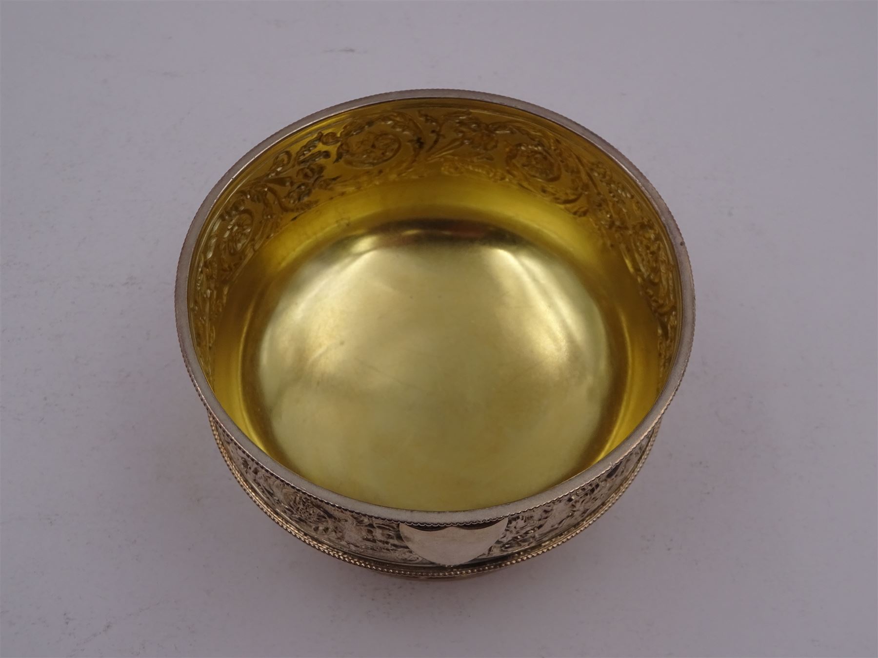 Victorian silver bowl, with embossed floral decoration and beaded rim, gilt interior and two applied shield cartouches, upon stepped circular foot, with a silver apostle spoon, with gilt bowl, both hallmarked George Unite, Birmingham 1883, bowl H5.5cm, within fitted tooled leather, silk lined case