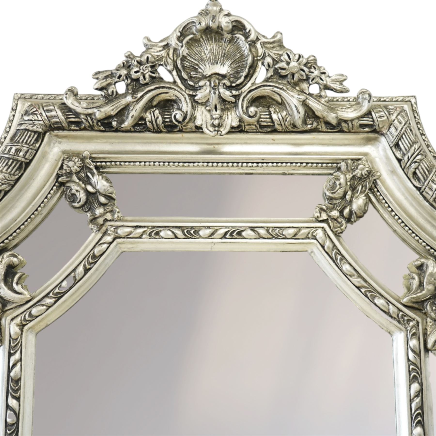 Impressive Baroque Revival mirror in antique silvered finish, the pierced cartouche shell pediment flanked  by C-scrolls and flower heads, the outer frame with ribbon-twist motifs throughout, the central arched bevelled plate surrounded by further rectangular mirror panels with cartouche mounts