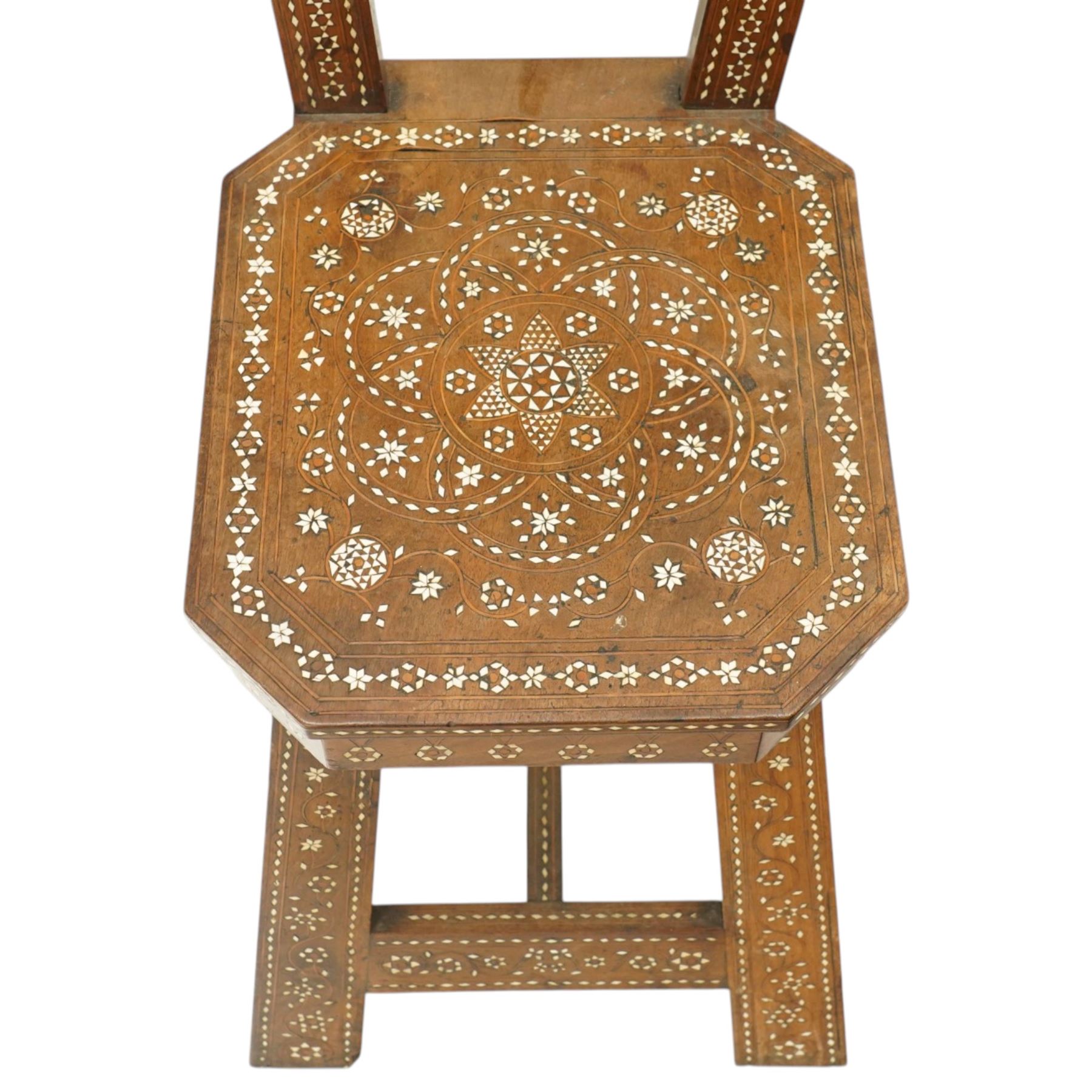 19th century Syrian olive wood and ivory inlaid chair, the shaped back and cresting above a panel centred by a circular starburst roundel within geometric and foliate marquetry and stringing, the tapering uprights and frame extensively inlaid with repeating ivory motifs, the octagonal seat similarly decorated, raised on splayed legs united by H-stretcher with further inlaid ornament