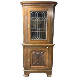 Arts & Crafts period oak corner cabinet, projecting cornice over astragal glazed door and single panelled door decorated with applied carved foliate scrolls and stylised roods surrounded by moulded edge, enclosing single shelf