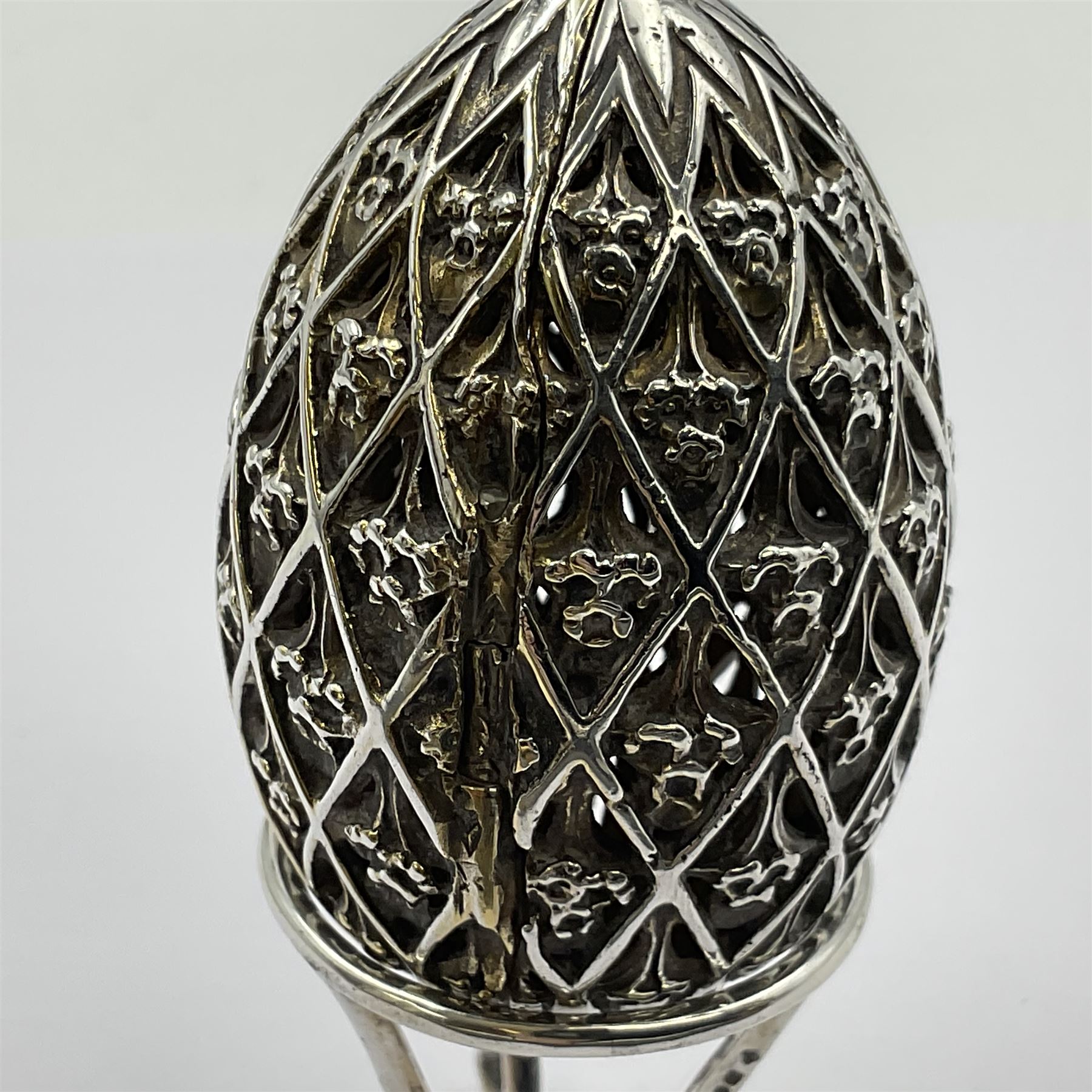 Modern silver limited edition Easter egg, no. 70/500, the openwork lattice body decorated with gilded panels of flower heads, opening to reveal a gilt interior, upon silver stand with three scrolling pad feet, each hallmarked St James House Company, London 1979, height including stand 8cm