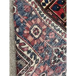Persian red and blue ground rug, overall geometric and stylised design, the field with repeating squares each decorated with stylised motifs, three band border, the main band decorated with stylised flower heads