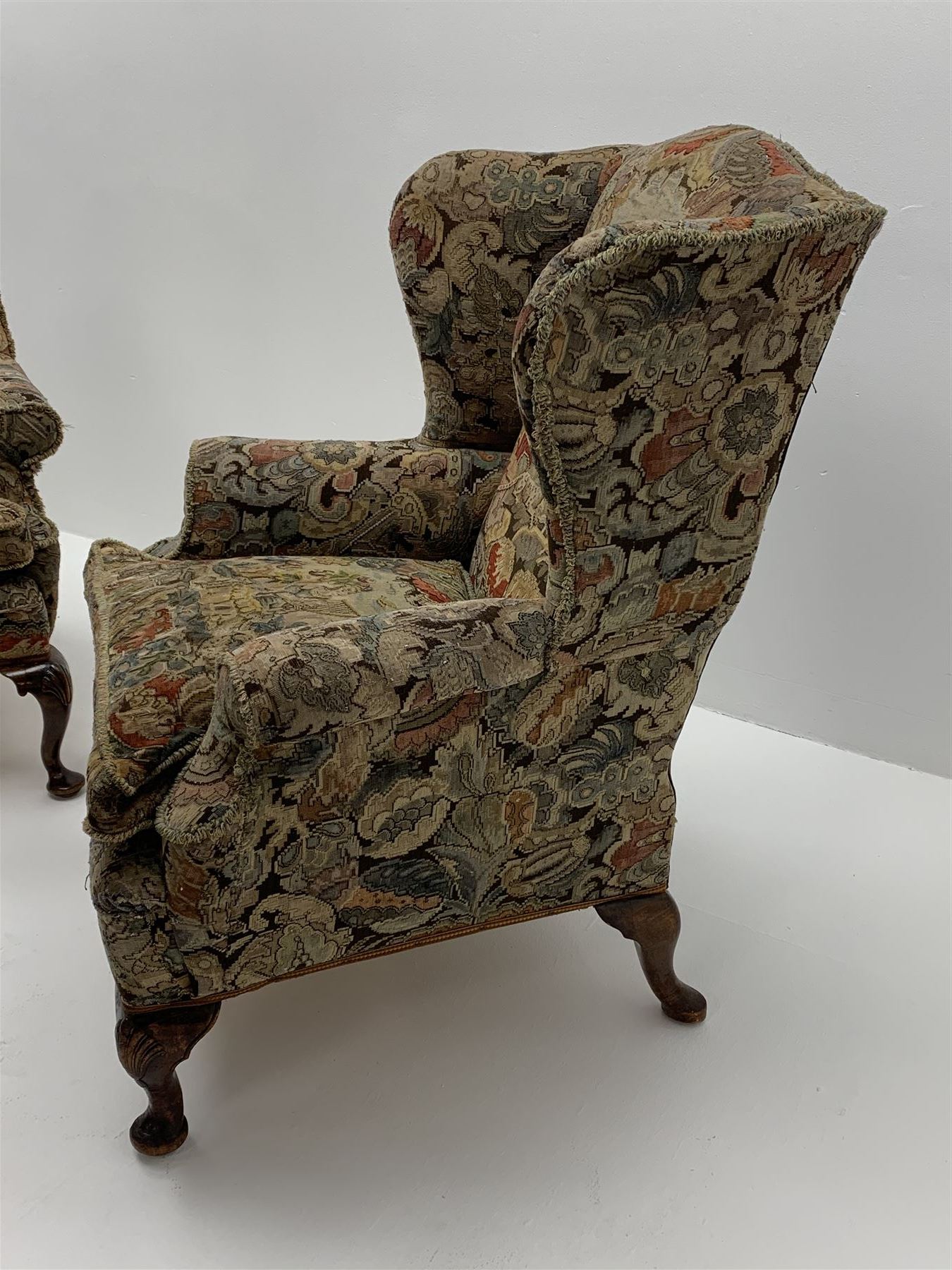 Matched pair early 20th century Queen Anne style wingback armchairs, walnut framed, sprung seats with seat cushions upholstered in needle work cover, shell carved cabriole front feet