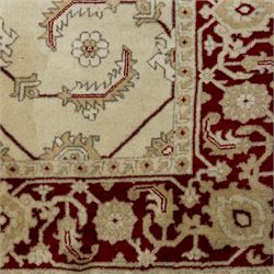 Baluchi signed hand-knotted rug, ivory ground, with an all-over geometric lattice design incorporating stylised flowerheads, hooked motifs and angular vine work, enclosed by a crimson border with repeating floral motifs and scrolling vines, flanked by narrow patterned guard stripes, signed to one corner, with cotton fringes