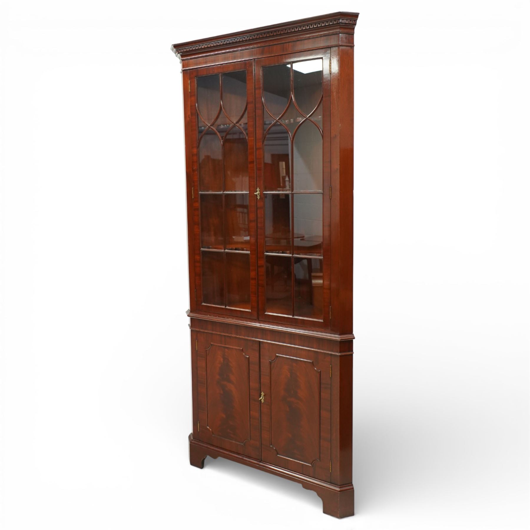 William Tillman - Early 20th century mahogany corner cabinet, the projecting moulded cornice with dentil detail over a glazed upper section enclosed by a pair of astragal glazed doors with Gothic arched tracery, the interior fitted with shaped shelves, above a moulded waist and a lower cupboard enclosed by two panelled doors with shaped fielded panels, raised on bracket feet