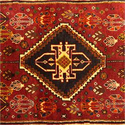 South West Persian Qashqai rug, hand knotted wool with central dark blue lozenge medallion containing geometric motifs, on a madder red field decorated with stylised floral boteh motifs, indigo spandrels, multiple borders of floral rosettes, from the region of Fars, south-west Persia