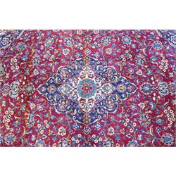 Central Persian Kashan hand-knotted carpet, crimson field with a central elaborate cusped medallion surrounded by elegant scrolling floral vine design incorporating stylized palmettes, rosettes and foliate sprays and similarly decorated spandrels enclosed by a dark indigo main border of floral arabesques between multiple guard stripes, cotton fringe ends 