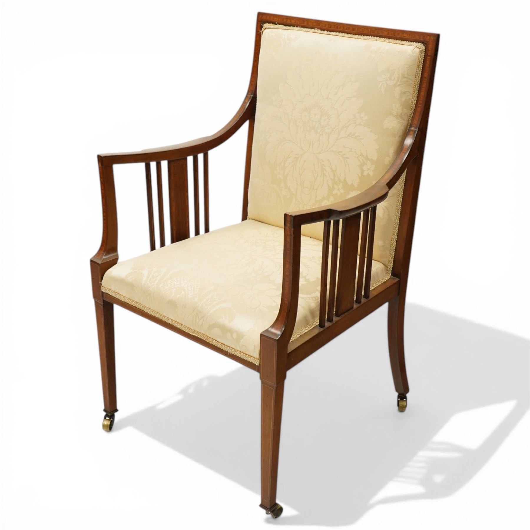 Arts & Crafts period inlaid mahogany framed armchair, swept arms with satinwood-strung supports over back and sprung seat upholstered in cream foliate damask fabric, on square tapering supports with castors