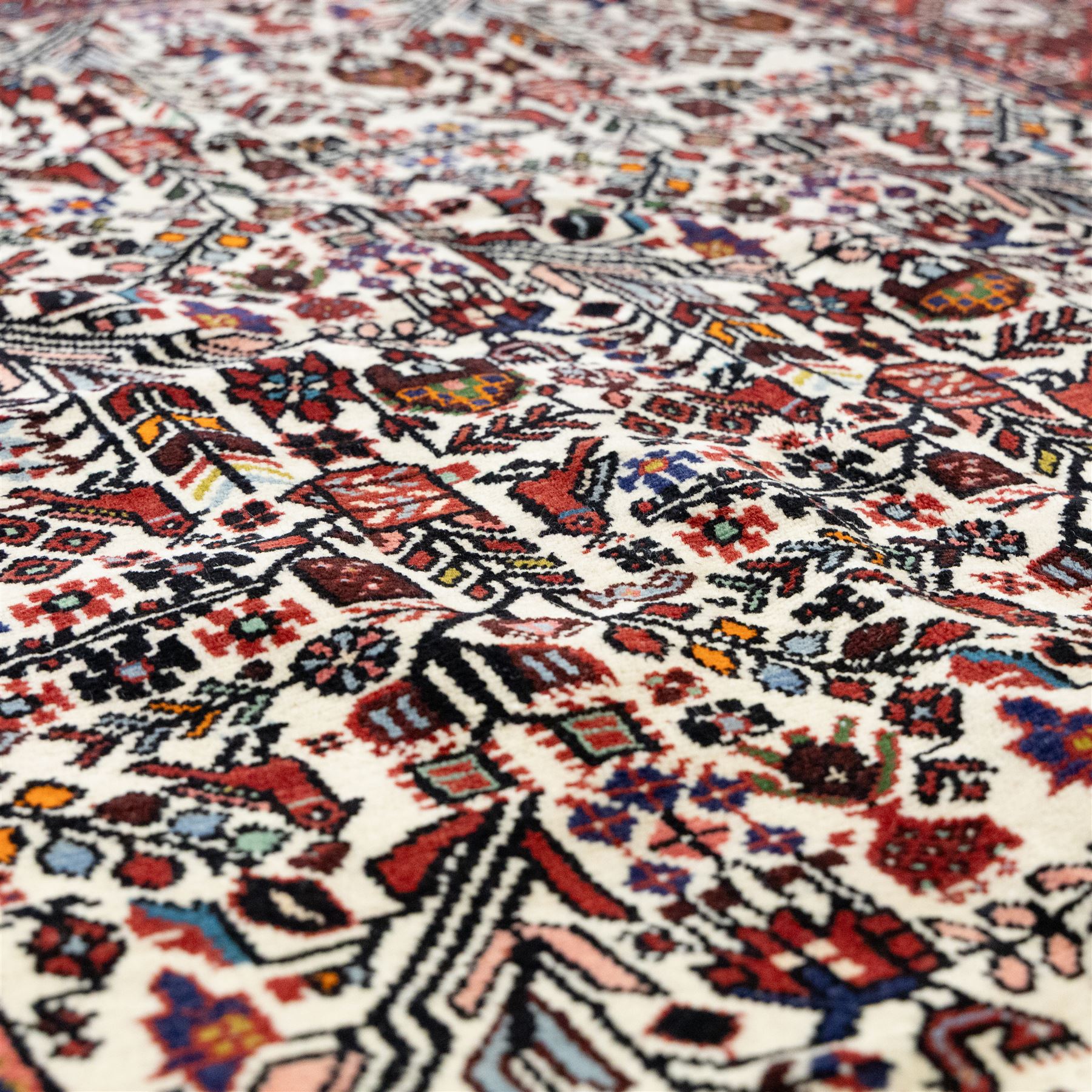 North west Persian Rudbar hand-knotted rug, ivory field woven with a repeating pattern of stylized shrubs, rosettes, and geometric floral motifs in tones of madder red, turquoise, indigo, and ochre, enclosed by a border of linked rosettes and angular flowerheads between narrow guard stripes 