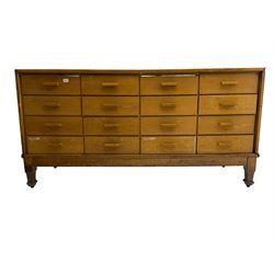 Early 20th century oak framed haberdashery shop counter, glass panel exterior enclosing sixteen graduating drawers with oak fronts and handles, raised on shaped tapering supports 