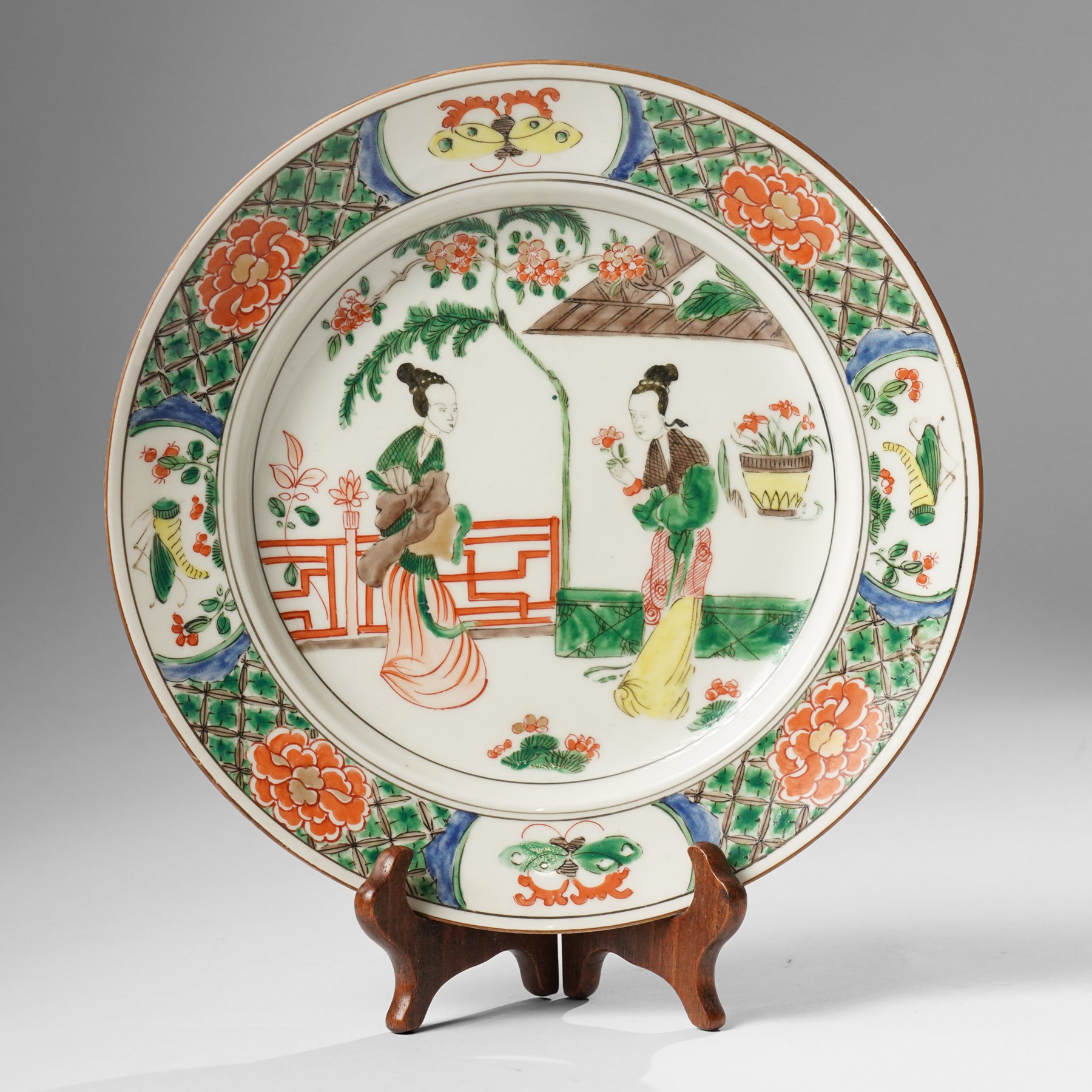 Chinese famille verte plate, painted with two ladies in a garden terrace setting, the border with butterfly and insect vignettes, D23cm 