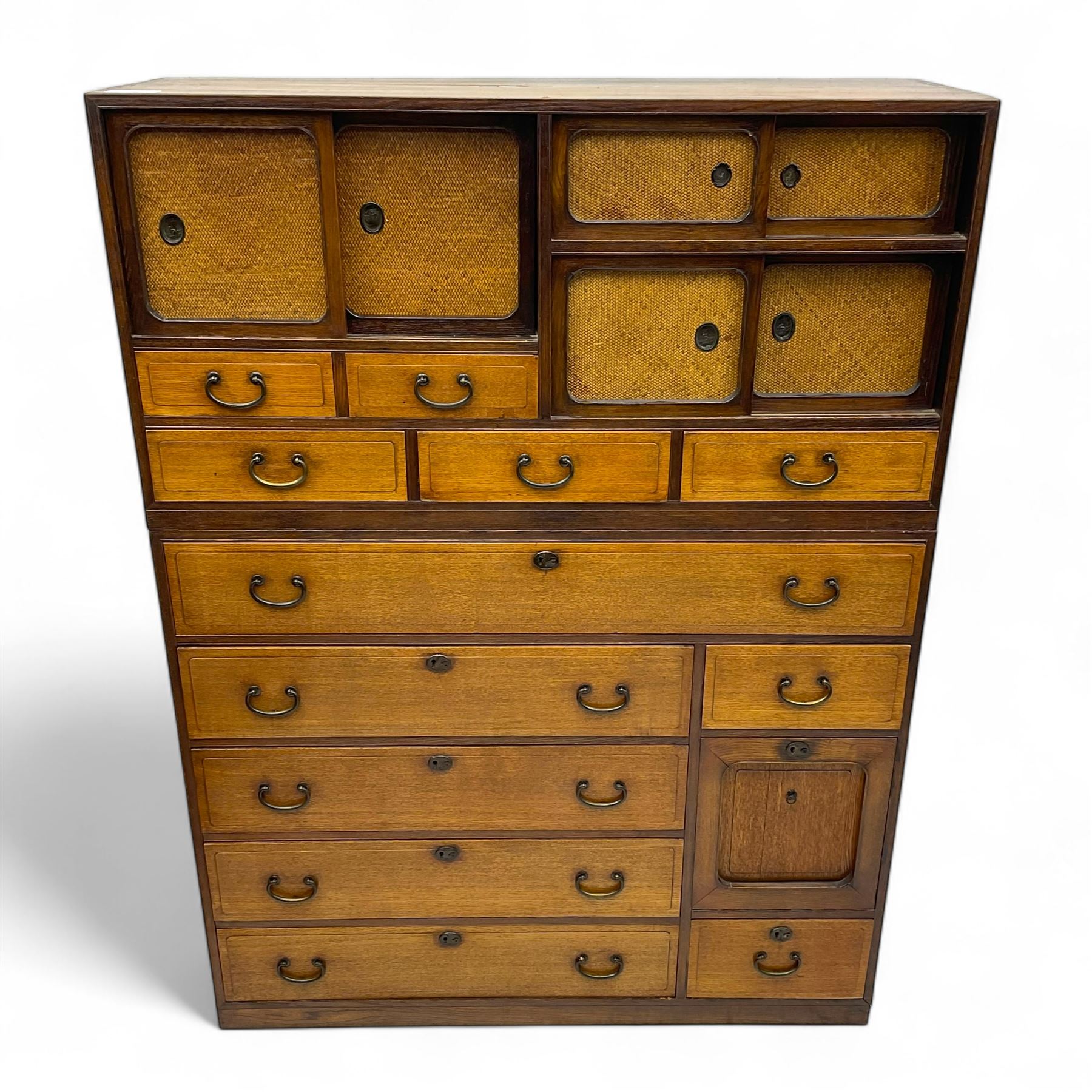Late Meiji-period Japanese keyaki wood tansu chest, upper section with six sliding woven rattan doors over five drawers, lower section fitted with an asymmetrical arrangement of seven drawers and side cupboard with a hinged door enclosing three additional drawers, iron drop handles to sides