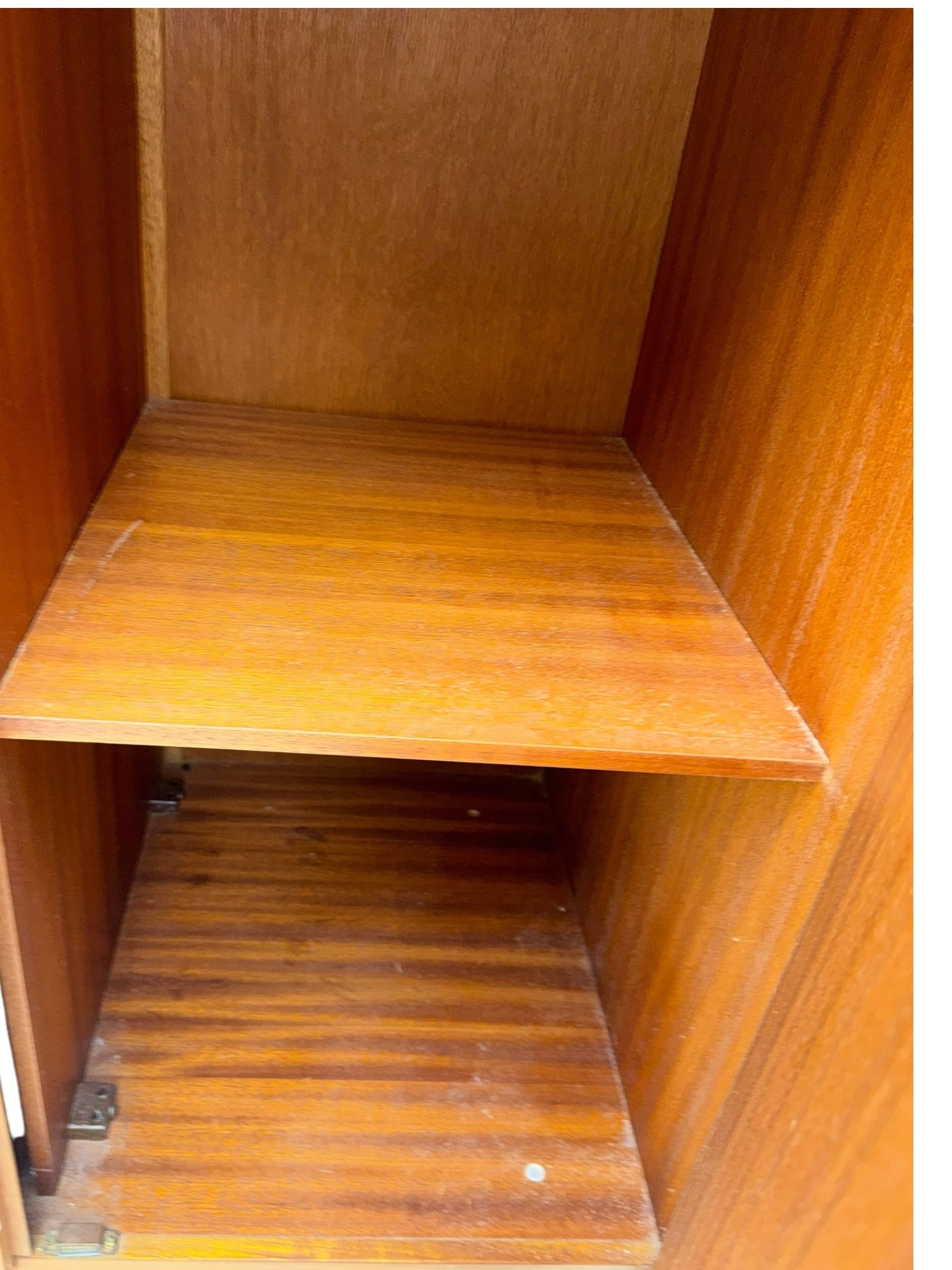 William Lawrence - mid-20th century teak double wardrobe, upper storage section over twin doors featuring recessed handles and contrasting horizontal panel, enclosing hanging rail compartment, towel rail, mirror, shelves and drawer, on plinth base with concealed castors