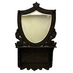 Early 20th century carved oak hall mirror, shield shaped bevelled glass plate, hat hooks, single shelf, Whitby Ammonite crest