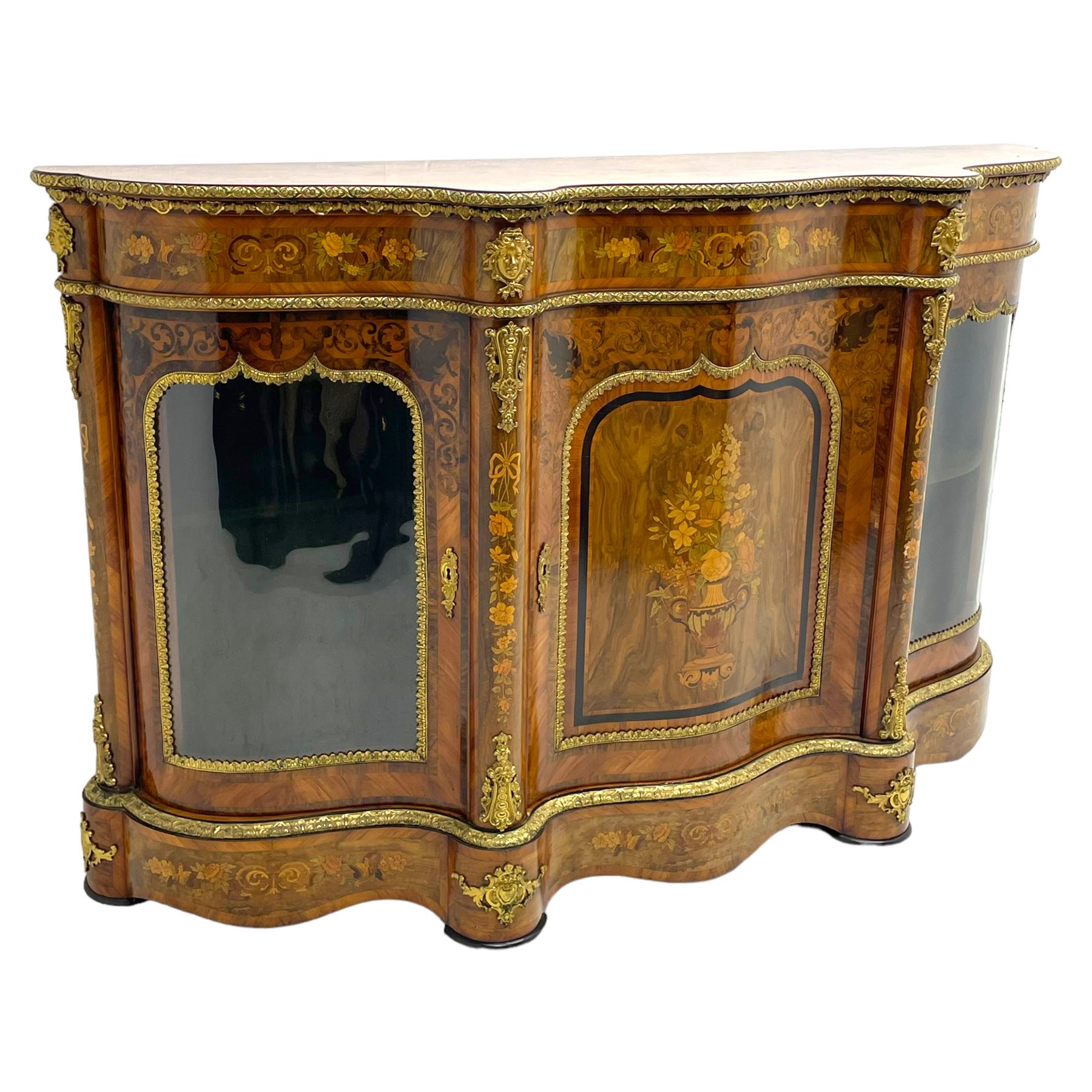 Victorian design inlaid figured walnut credenza sideboard, shaped form with crossbanded and book-matched top, the frieze rails inlaid with foliage scrolls and flower heads, central panelled door inlaid with floral urn flanked by two glazed doors, on shaped plinth base inlaid with foliate decoration, mounted by cast gilt metal masks and floral egg and dart beading 