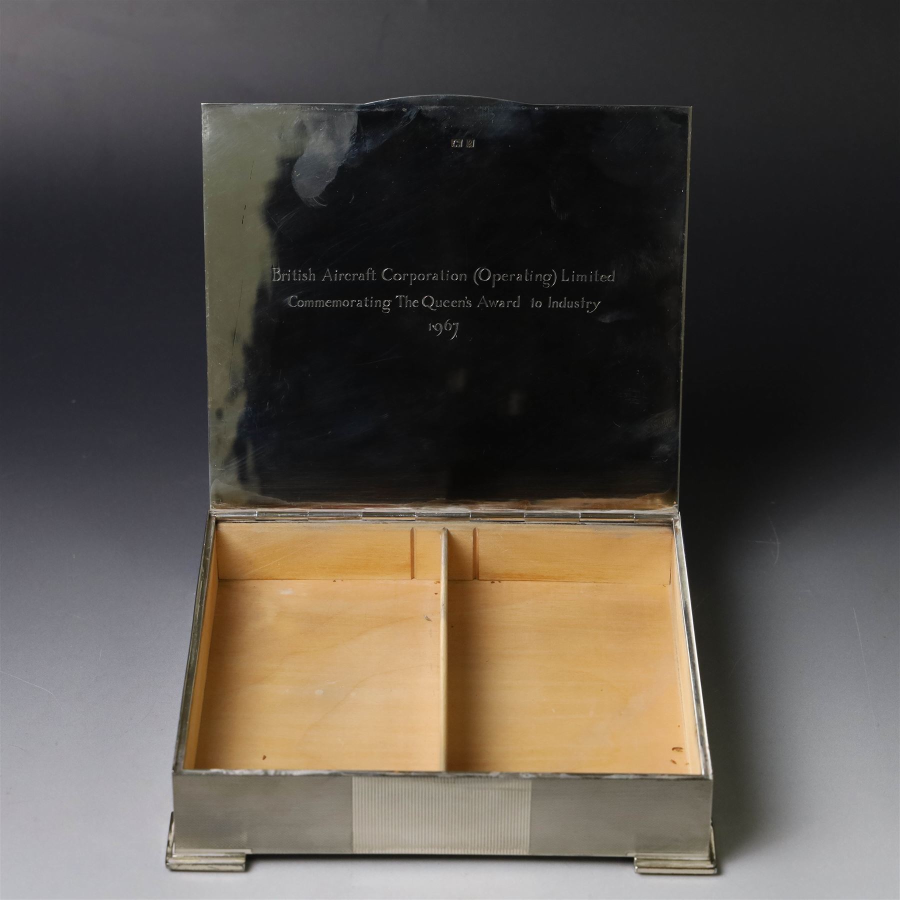 1960s silver mounted cigarette box, of rectangular form with engine turned decoration, upon four bracket feet, with presentation engraving to interior lid reading  'British Aircraft Corporation (Operating) Limited Commemorating the Queen's Award to Industry 1967, hallmarked James Geraghty, Birmingham 1965, with retailers mark for Asprey, W16.5cm, H4.5cm, in Garrard & Co Jewellers box