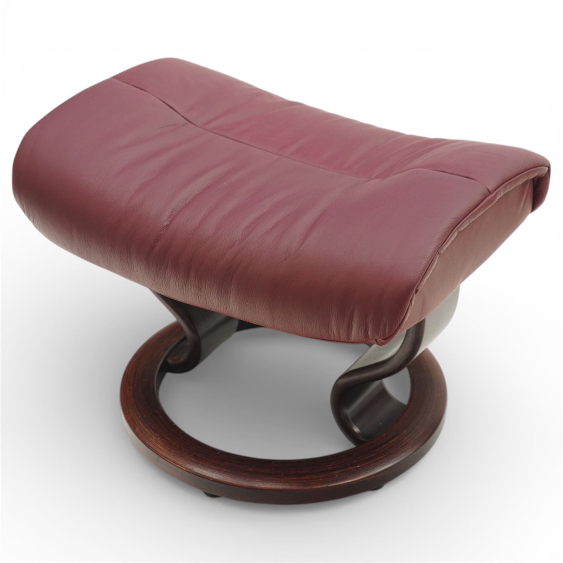 Ekornes - Stressless reclining armchair and matching footstool, upholstered in oxblood leather with padded headrest and segmented back cushion, shaped armrests with exposed adjustment handles, raised on stained laminated beech circular swivel base, the conforming stool on matching ring base