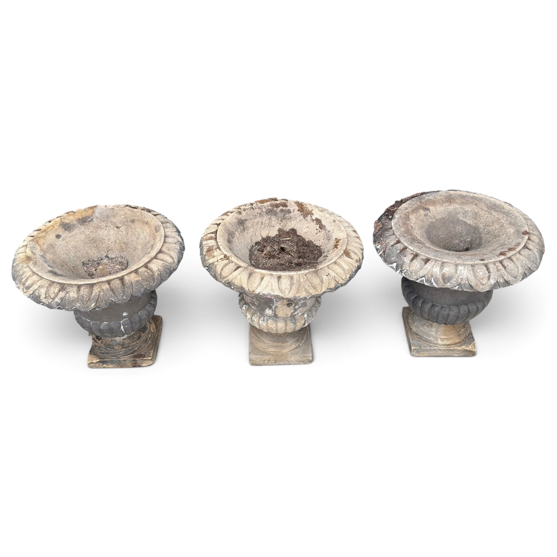 Set of three 19th century weathered carved sandstone garden urns of Neoclassical campana form, the broad everted rim carved with pointed egg-and-dart motifs, above a plain waisted bowl with gadrooned underbelly, on moulded rope-twist socle and square plinth base