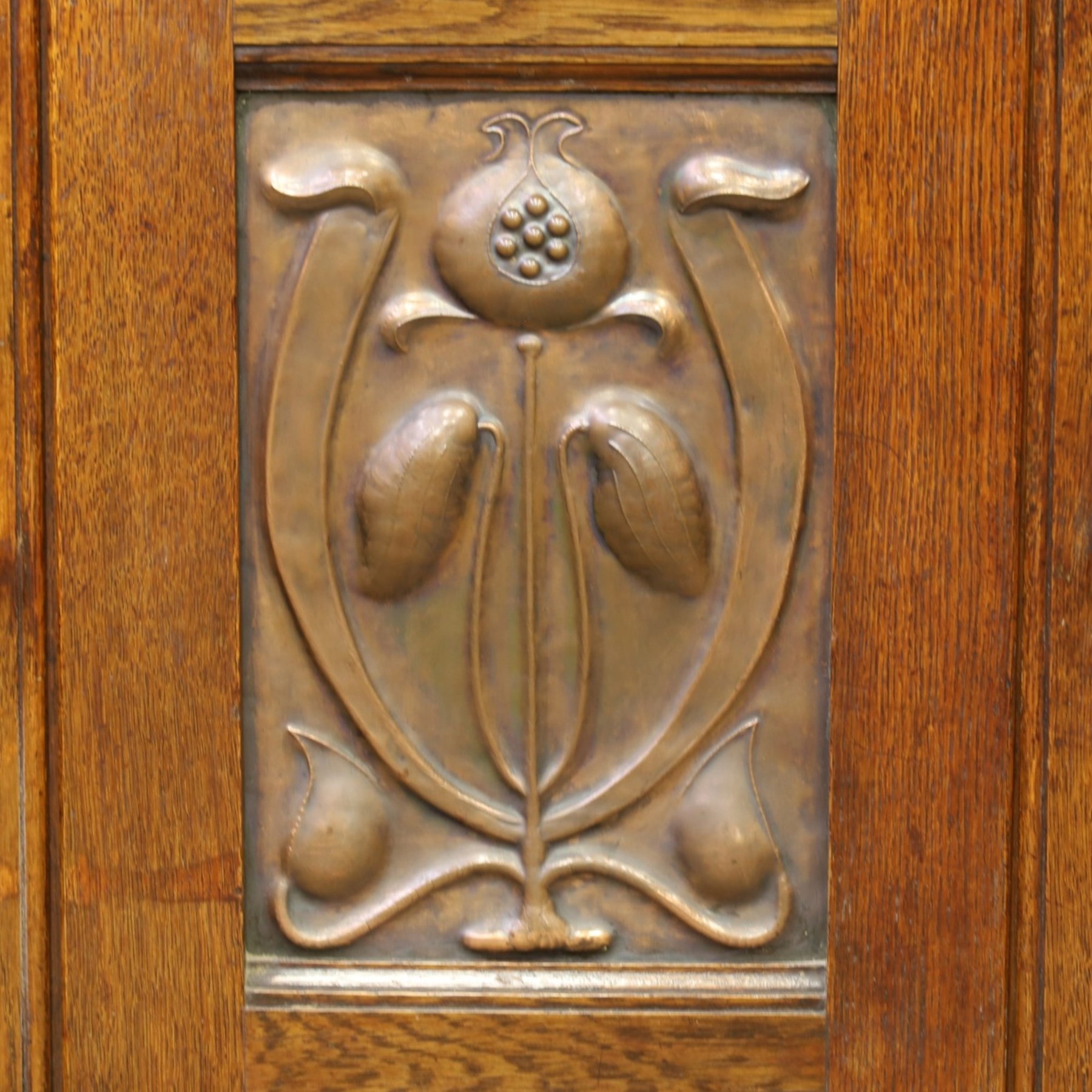 Art Nouveau oak mirrored sideboard, in the manner of Liberty's London, the raised back fitted with bevelled mirror plates divided by turned supports beneath a projecting cornice, above two drawers and panelled cupboard doors, the central panel applied with stylised floral carved panel, raised on shaped feet